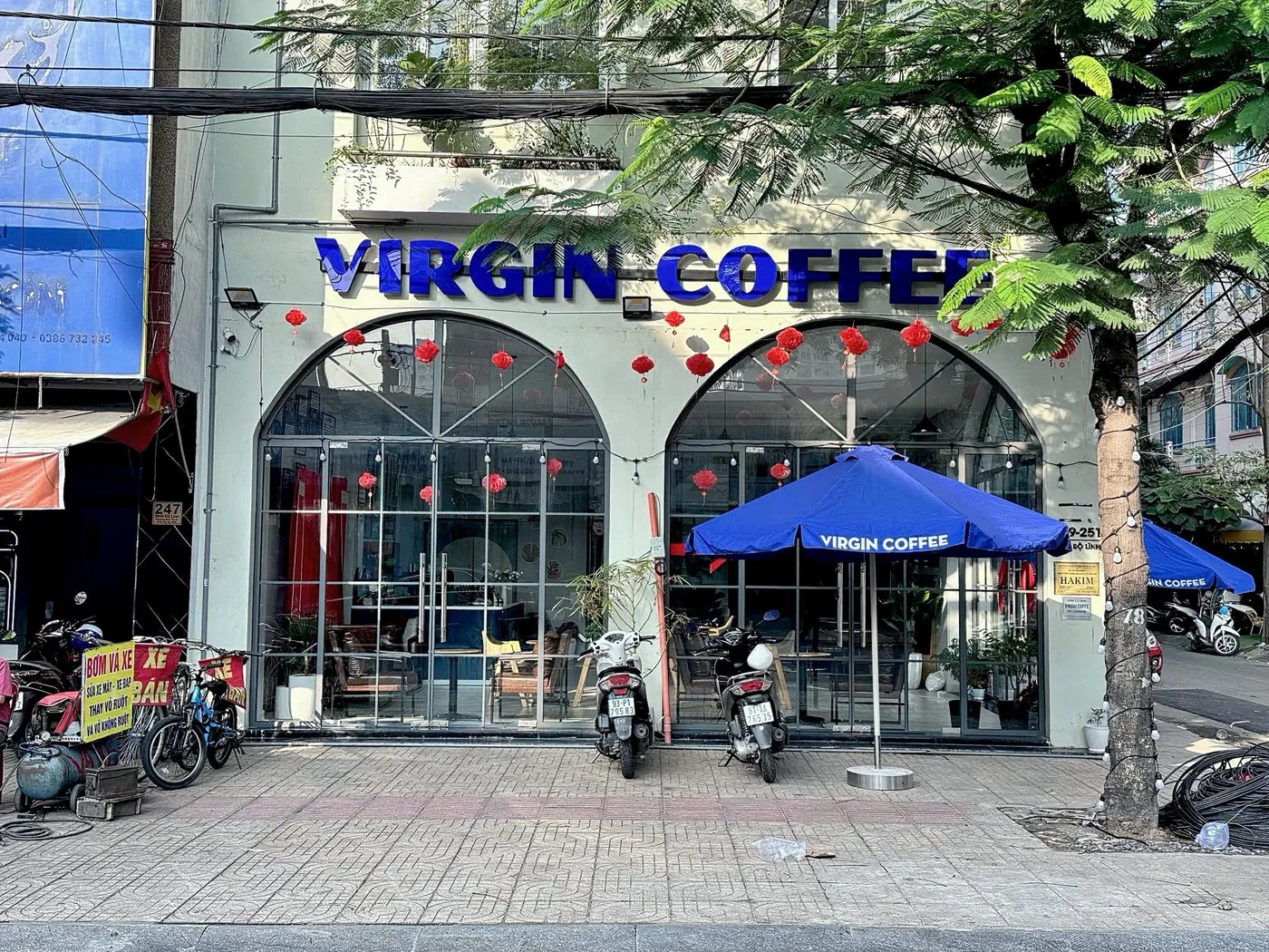 The first Virgin Coffee in Bình Thạnh — two arched glass windows under a blue sign, a blue umbrella on the pavement.