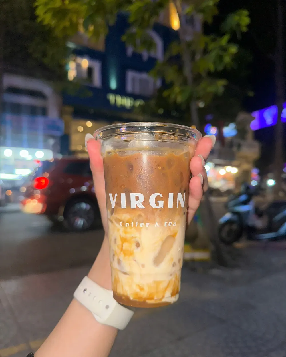 An iced coffee in a Virgin cup, held on Nguyễn Thái Bình outside the café at night.