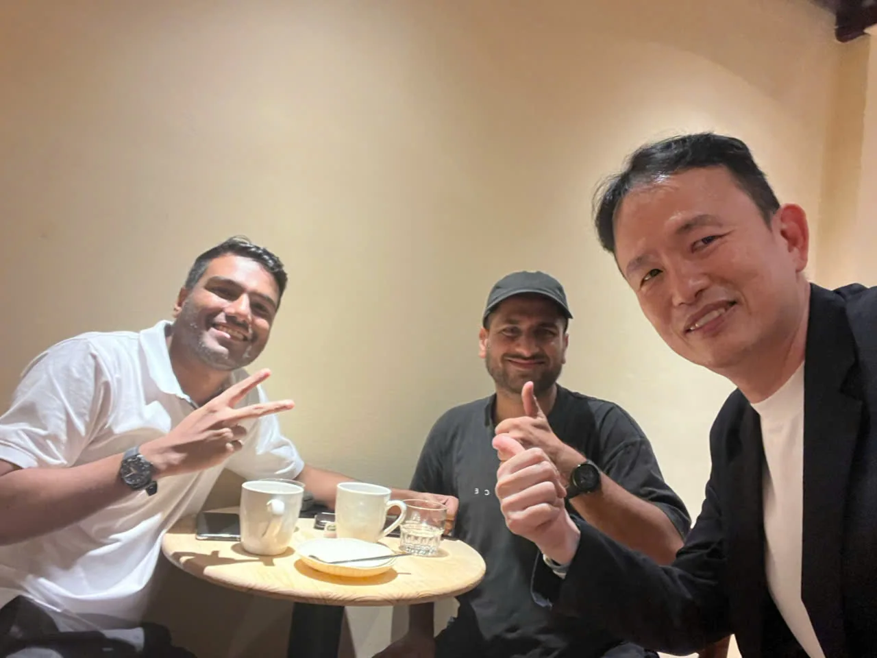Three guests around a small round table with cups of coffee, gesturing to the camera.