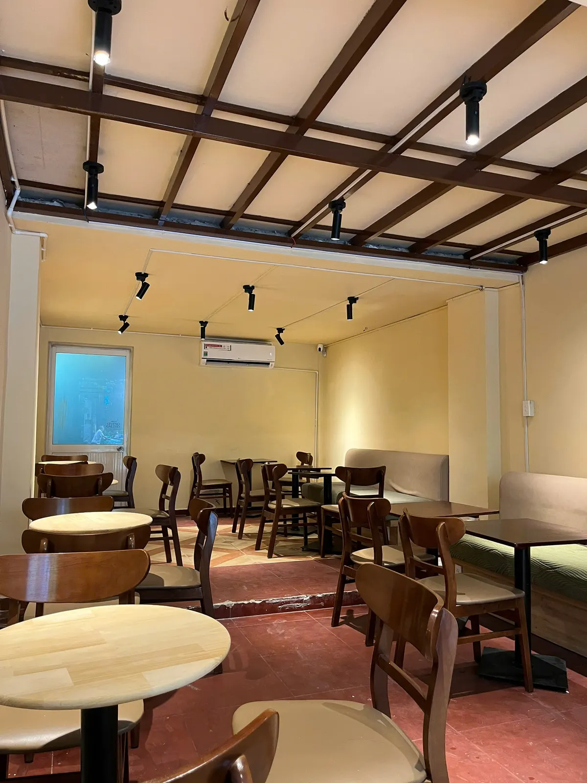 The room at Virgin Saigon Original Coffee seen from the door — timber-lattice ceiling, green banquette, air conditioning on the wall.