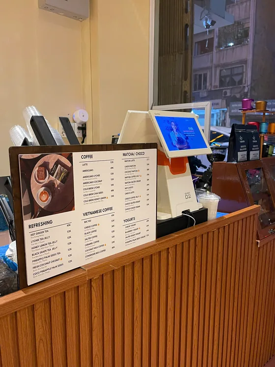 The service counter, with the printed drinks board propped on it and the till behind.