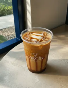 Iced caramel coffee in the Virgin cup, golden milky coffee over ice with amber caramel streaks down the inside of the cup and a caramel ribbon on the foam.