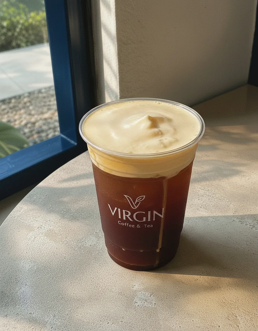 Iced cheese coffee in the Virgin cup, deep reddish-brown coffee under a thick ivory cheese-cream cap with a cream drip down the side.